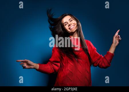 Photo portrait of girl smiling dancing overjoyed at party in red sweater isolated on dark blue color background Stock Photo