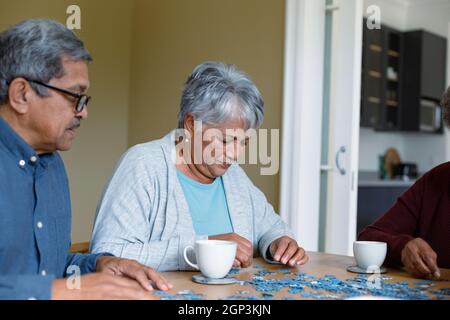 Two diverse female and male friends sitting at table and doing puzzles Stock Photo