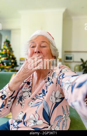Happy caucasian senior woman wearing santa hat having video call, sending kisses at christmas time Stock Photo