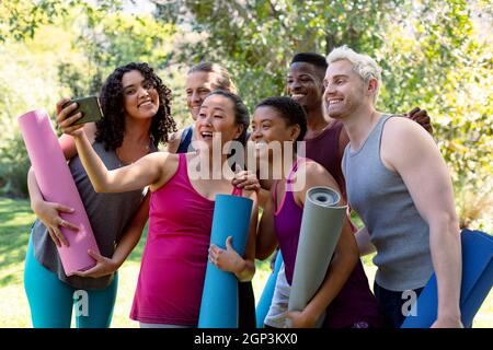 Group of happy fit diverse female and male friends holding yoga mats and taking selfie Stock Photo