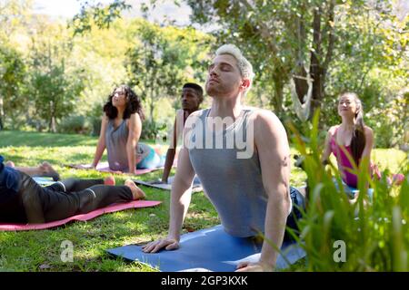 Group of diverse female and male people practicing yoga outdoors Stock Photo