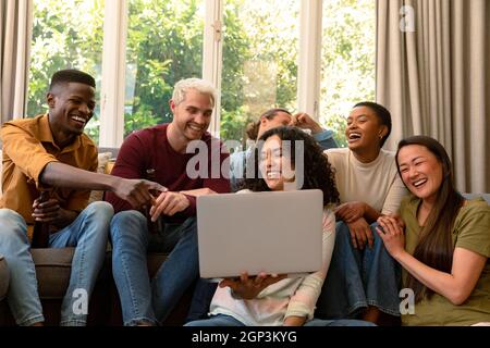 Group of happy diverse female and male friends drinking beer together and using laptop Stock Photo