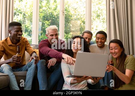 Group of happy diverse female and male friends drinking beer together and using laptop Stock Photo