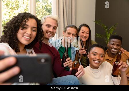 Group of happy diverse female and male friends drinking beer together and taking selfie Stock Photo