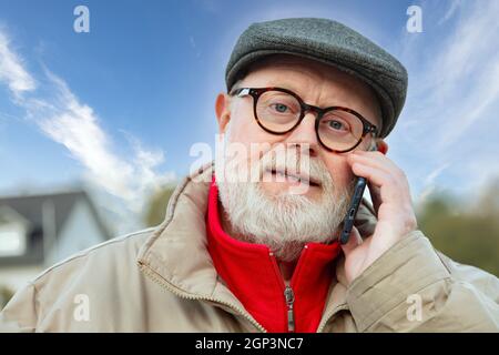 Man with cap in winter clothes using cell phone outdoor. Stock Photo