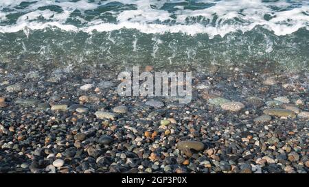Sea surf on a sunny day. Light waves, pebble shore. Multi-colored wet pebbles on the shore Stock Photo