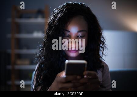 African Woman Using Mobile Phone Or Smartphone In Dark At Night Stock Photo