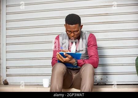 young businessman sitting outside is writing on note book Stock Photo