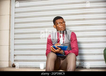 young businessman sitting outside is thinking about a new project and holding a document and a pen Stock Photo