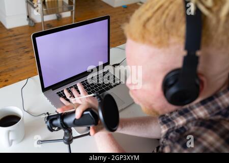 Happy albino african american man with dreadlocks working from home and making podcast Stock Photo