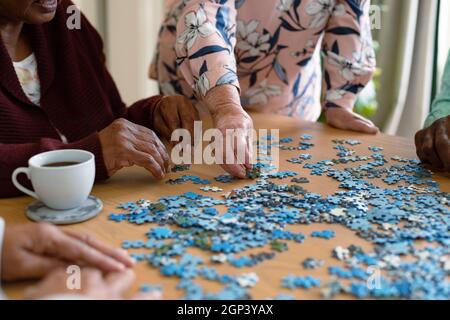 Hands of two diverse senior women and african american male friend doing puzzles Stock Photo