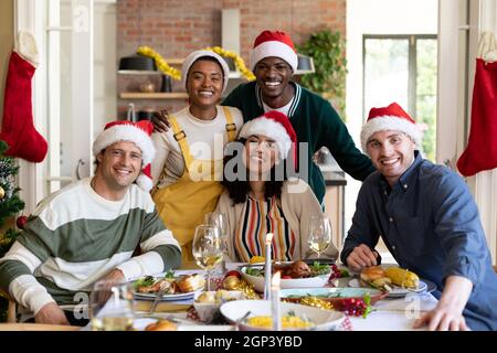 Group of happy diverse female and male friends in santa hats , celebrating christmas, taking photo Stock Photo