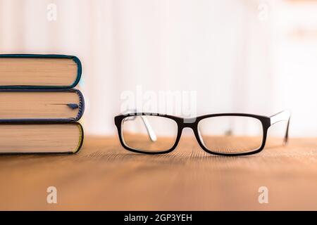 Stack of books and glasses lying on wooden desk at home. Knowledge and science Stock Photo