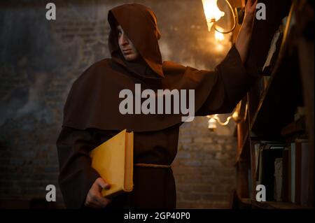 Male exorcist in black hood holding a torch. Exorcism, mystery paranormal ritual, dark religion, night horror, potions on shelf on background Stock Photo
