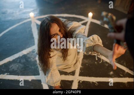 Male exorcist in black hood casting out devil from scary woman. Exorcism, mystery paranormal ritual, dark religion, night horror Stock Photo