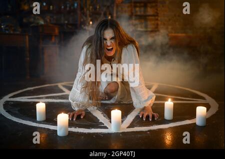 Crazy demonic woman sitting in magic circle with candles, demons casting out. Exorcism, mystery paranormal ritual, dark religion, night horror, potion Stock Photo