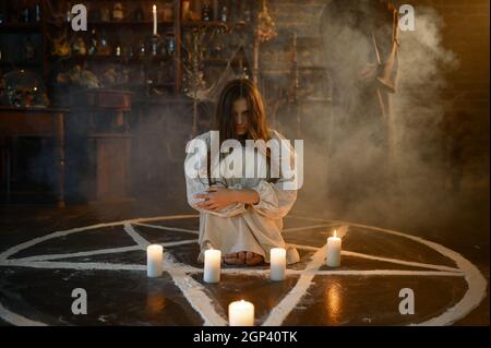 Crazy demonic woman with pumpkin sitting in magic circle with candles, demons casting out. Exorcism, mystery paranormal ritual, dark religion, night h Stock Photo