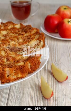 Apple pie on a plate on a wooden table against a background of red apples. Stock Photo