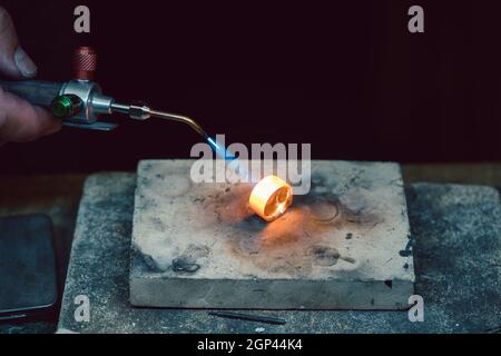 Goldsmith or jeweler heating up a ring with blue flame to work on that piece of jewelry Stock Photo
