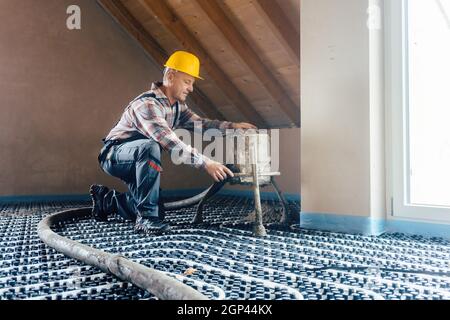 Worker on construction site installing pipes for underfloor heating system kneeling on the floor Stock Photo