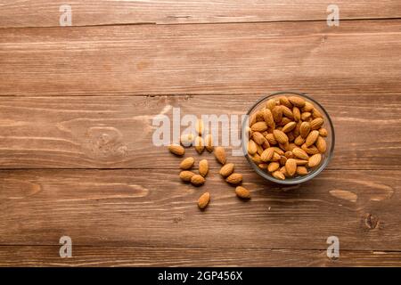 Background from almond nuts. Peeled almond kernels on a brown board and in a transparent cup. Top view, close-up. Stock Photo