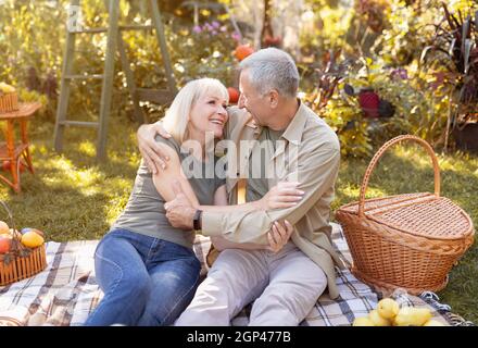 Loving senior married spouses resting in autumn park, having picnic and embracing, chatting and laughing, enjoying evening outdoors, free space Stock Photo
