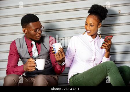 Young business people sitting outside sharing coffee during break while smiling. Stock Photo