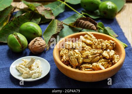 Young walnuts, shelled and in shell, walnut leaves. Rustic style. Stock Photo