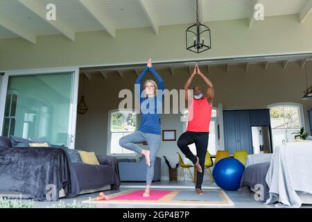 Happy senior diverse couple in exercise clothes practicing yoga together, meditating Stock Photo