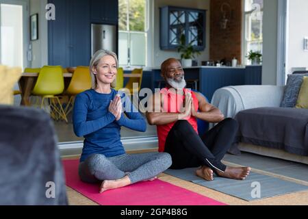 Happy senior diverse couple in exercise clothes practicing yoga together, meditating Stock Photo