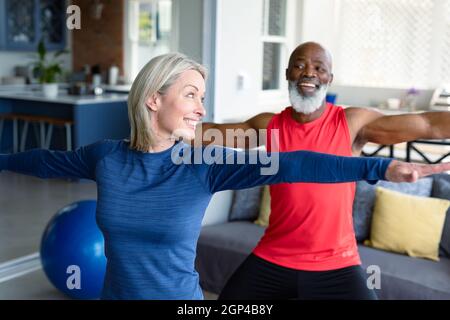 Happy senior diverse couple in exercise clothes practicing yoga together, stretching Stock Photo