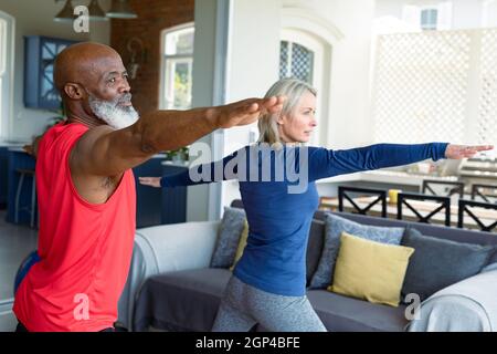 Happy senior diverse couple in exercise clothes practicing yoga together, stretching Stock Photo