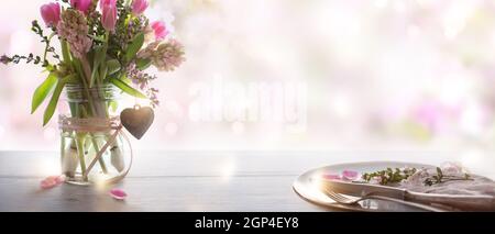 Table decorating with spring flowers and place setting for a wedding menu on gray wooden table, in background tender romantic pink bokeh with space fo Stock Photo