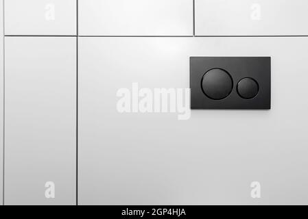 Black matt toilet flush with two round buttons placed in the wall of a restroom lined with a wooden panel. Stock Photo