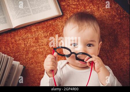 One year old baby among books with spectackles.Happy little child reading Stock Photo