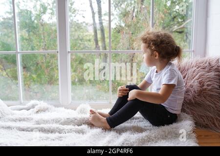Adorable little girl sitting on the windowsill at home Stock Photo