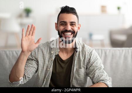 Online communication, video call and internet meeting concept. Positive young Arab man calling his friend on webcam, speaking to family remotely from Stock Photo