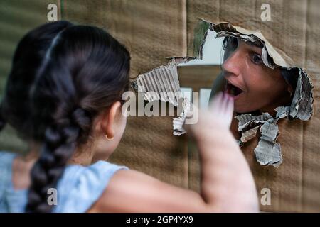 Woman with open mouth looking at a girl through a large hole in a carton. Stock Photo