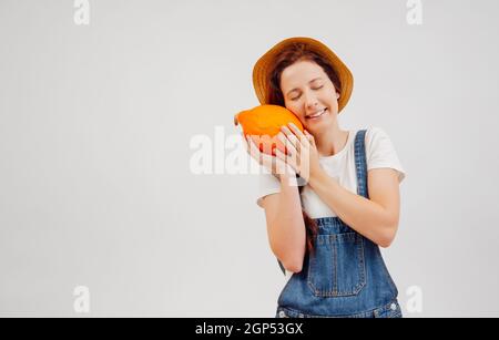 Woman in overalls and a hat presses a ripe orange pumpkin. Stock Photo