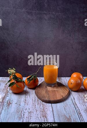 Large glass of orange juice on wooden table with several oranges marble background wooden floor Stock Photo