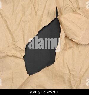 brown sheet of paper with a torn hole and a curled strip, black background Stock Photo