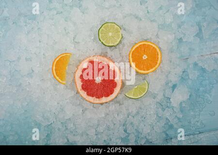 Close up fresh juicy citrus fruits slices, pink grapefruit, orange and green lime, over background of crushed ice, elevated high angle view, directly Stock Photo