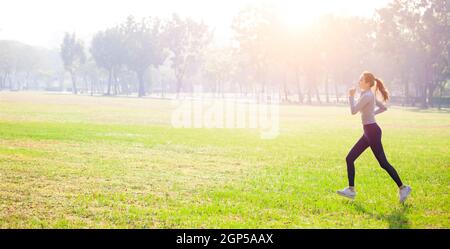 Young beautiful woman running on grass field at morning Stock Photo