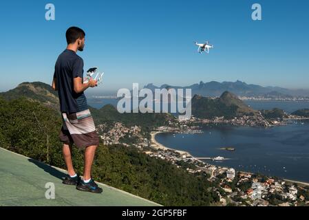 Niteroi, RJ, Brazil - July 5, 2016: Young man controlling a drone in a park with a beautiful view of Rio de Janeiro city. Stock Photo