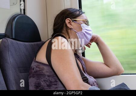 Barcelona, Spain - September 21, 2021: Exhausted woman take a nap on the train during her way to home. She is using a protective face mask due to coro