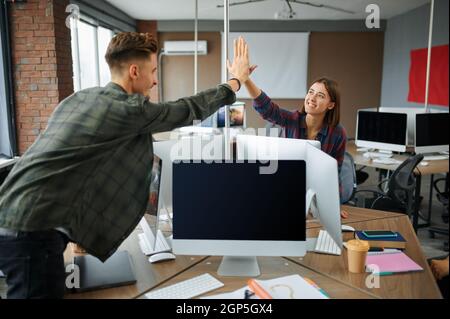 IT specialists high-five each other in office. Web programmer or designer at workplace, creative occupation. Modern information technology, corporate Stock Photo