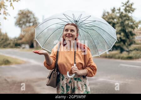 A beautiful girl stands under a transparent umbrella and stretches out her hand, catching drops of water. Horizontal banner, copy space Stock Photo