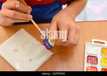 A girl paints a figurine made of salt dough with a brush Stock Photo