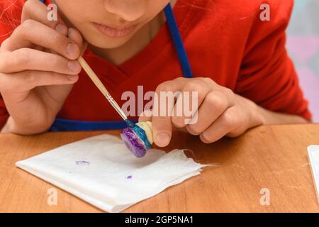 A girl paints a figurine made of salt dough with a brush, close-up Stock Photo