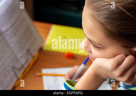 Close-up of a girl doing homework, a girl lost in thought distracted from the task Stock Photo